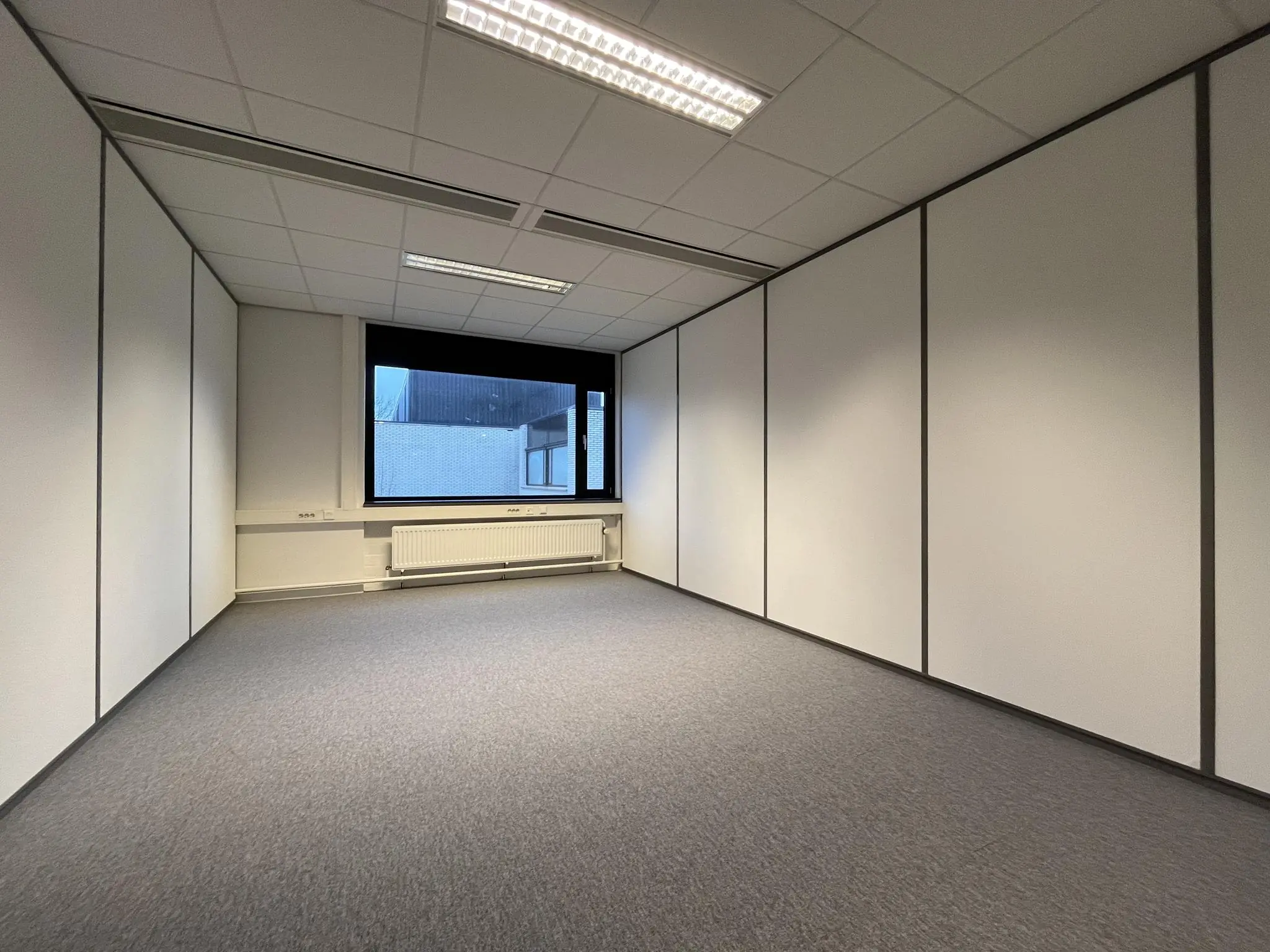 Leeg kantoorruimte met systeemplafond, grijze vloerbedekking en groot raam aan de Burgemeester Verderlaan.